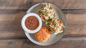 Traditional Sopes with a thick corn base topped with refried beans, crumbled cheese, lettuce, sour cream, and a choice of meat, served with a side of salsa.