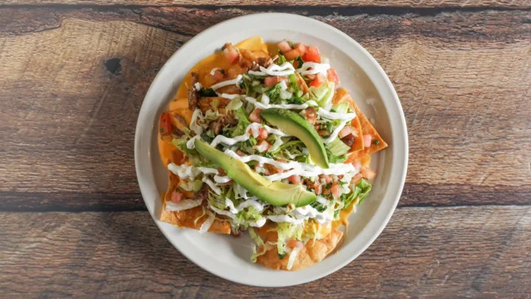 Ultimate Nachos: "A loaded plate of ultimate nachos piled high with melted cheese, seasoned beef, jalapeños, fresh guacamole, sour cream, and salsa, offering a burst of flavor in every bite."