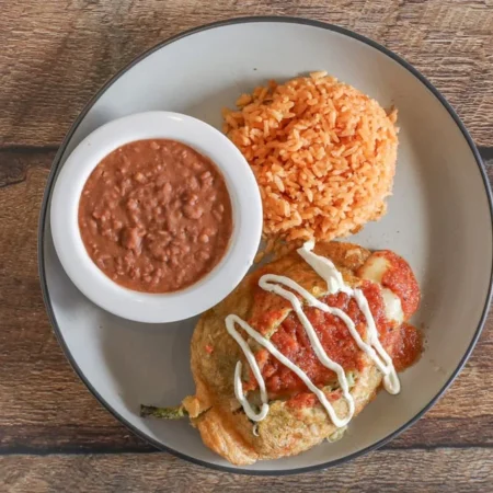 Chili Relleno stuffed with melted cheese, topped with a rich tomato sauce, and garnished with fresh cilantro, served with a side of rice and beans.