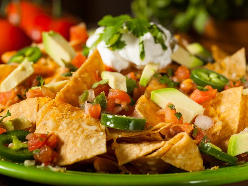 Ultimate Nachos: "A loaded plate of ultimate nachos piled high with melted cheese, seasoned beef, jalapeños, fresh guacamole, sour cream, and salsa, offering a burst of flavor in every bite."